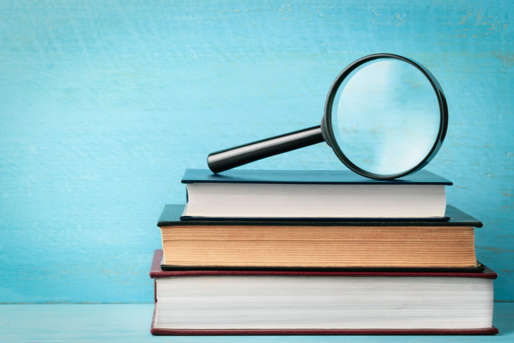 A magnifying glass on a stack of books on a blue wooden bookshelf with space for text